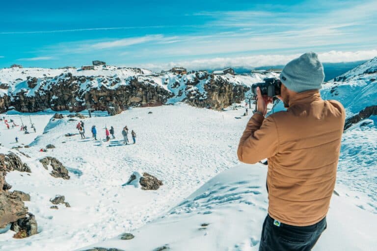 A man with a camera pointing at a group of people on a snow-covered mountain.