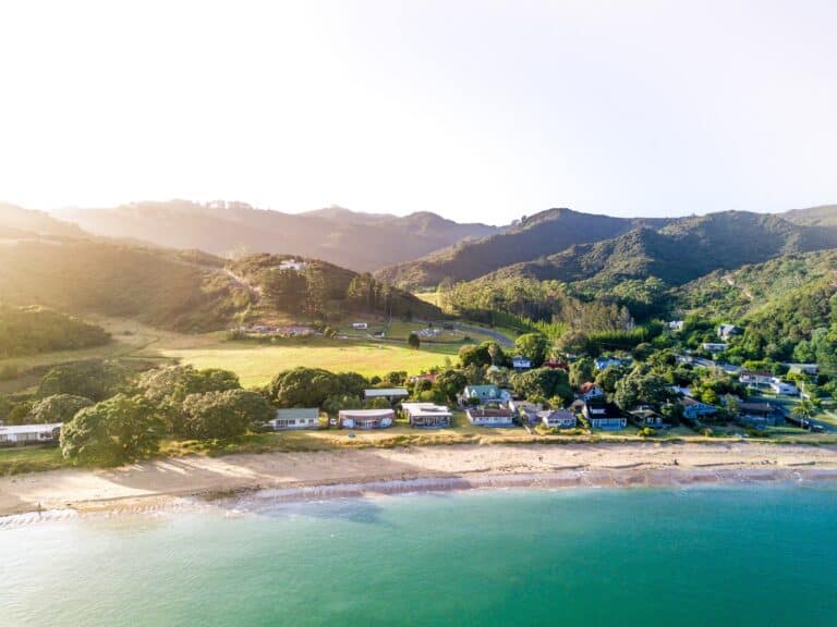 A beach with bright blue water against green mountains in New Zealand, which is worth visiting.