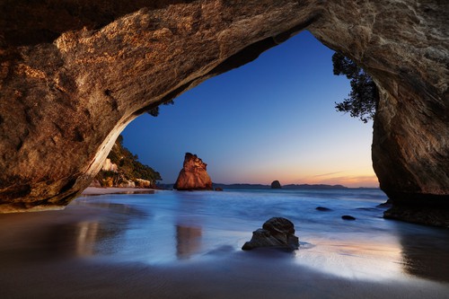 Cathedral Cove at sunrise, Coromandel Peninsula, New Zealand. The cheapest time to visit New Zealand would be in May when there are cooler temperatures.