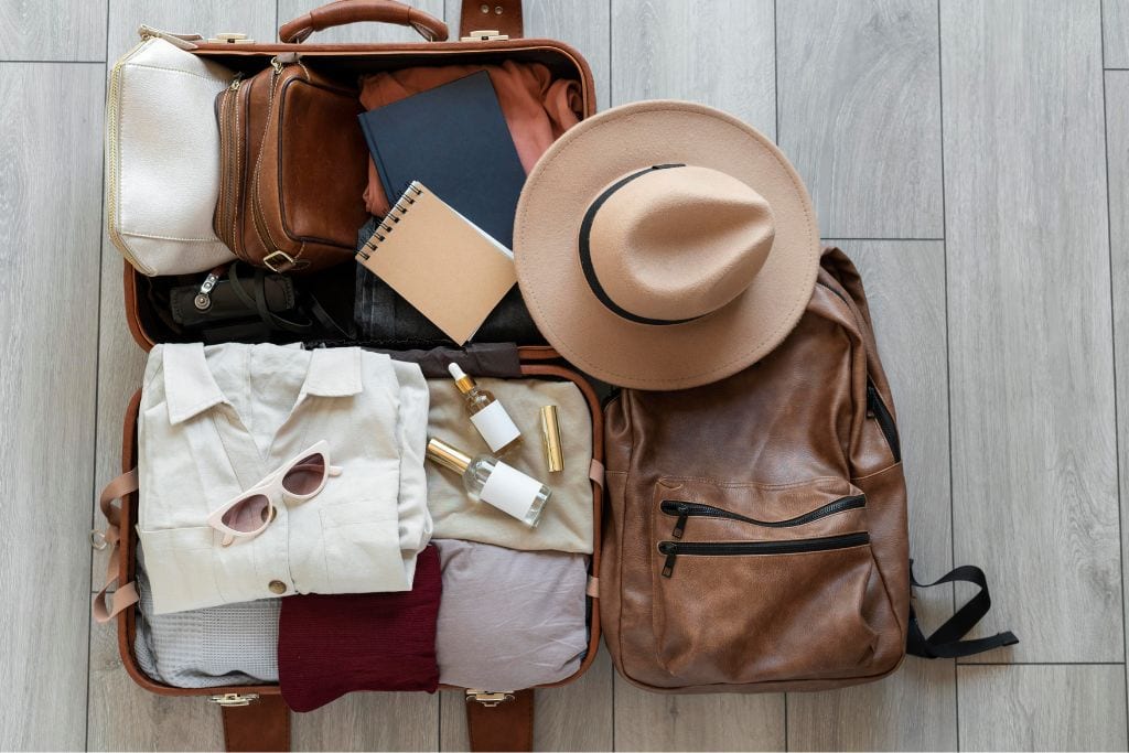 A brown leather suitcase with clothing, sunglasses, a hat, and more for packing for Paris in May.