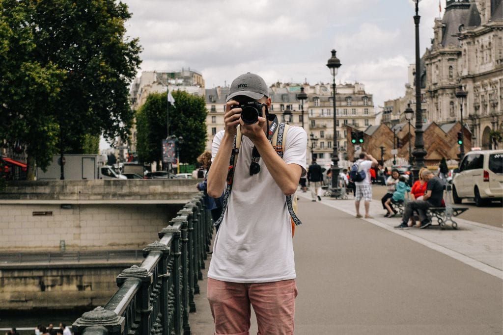 A man holding and aiming a camera on a bridge in Paris.