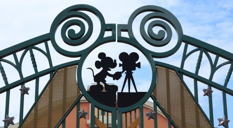 The gates of Disney with a silhouette of Mickey Mouse filming with a camera.