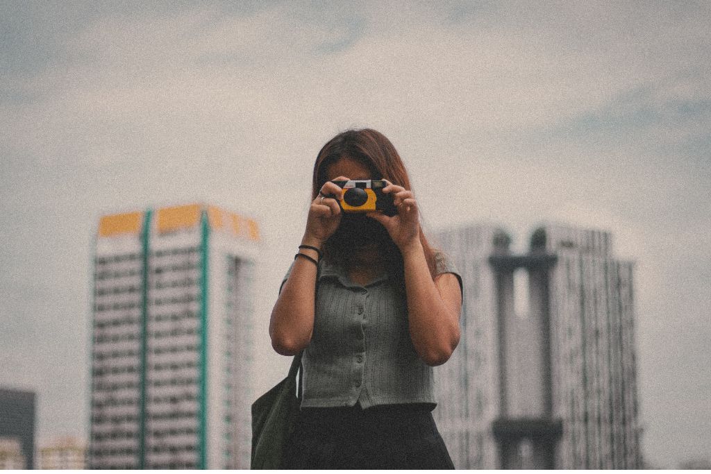 A girl pointing a disposable camera at the photographer. 