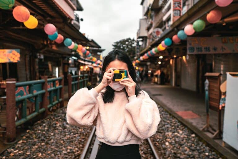 A woman looking at the camera while taking a picture with a disposable camera.