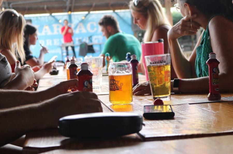 People drinking beer while sitting at a big table at an outdoor bar.