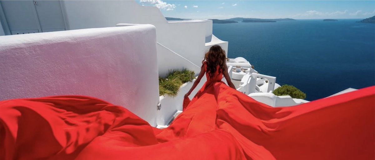 A woman with her back to camera in a flowing bright red dress in Greece.