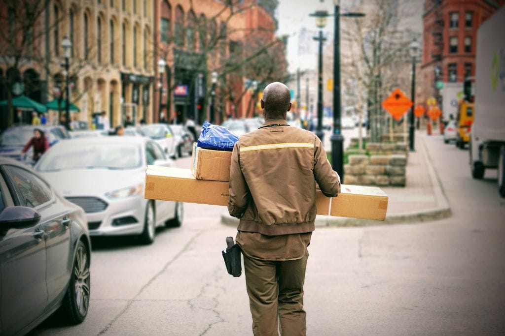 An Amazon delivery man walking down a city street carrying two packages. Is there Amazon in France? Yes, Amazon has a dedicated Amazon website for France.