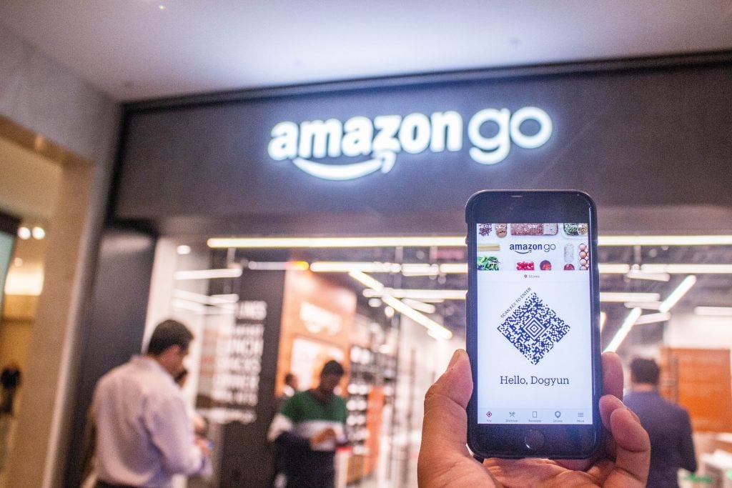 A hand holding up a cellphone with an Amazon QR code on it with an Amazongo store in the background.