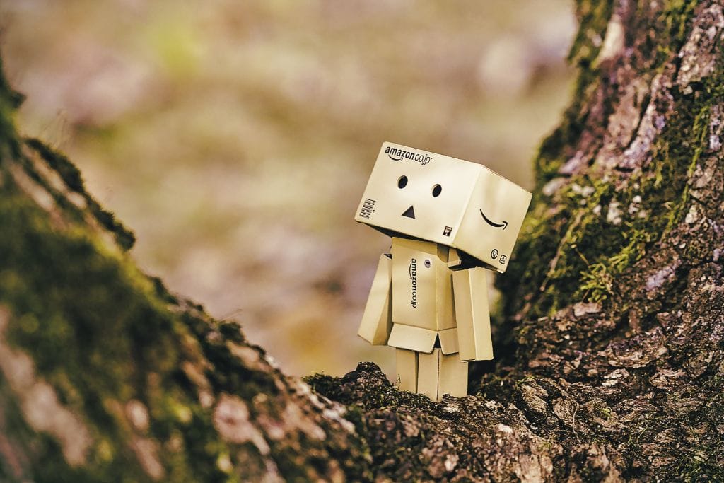 A little robot made from Amazon brown packages sitting the nook of a tree.
