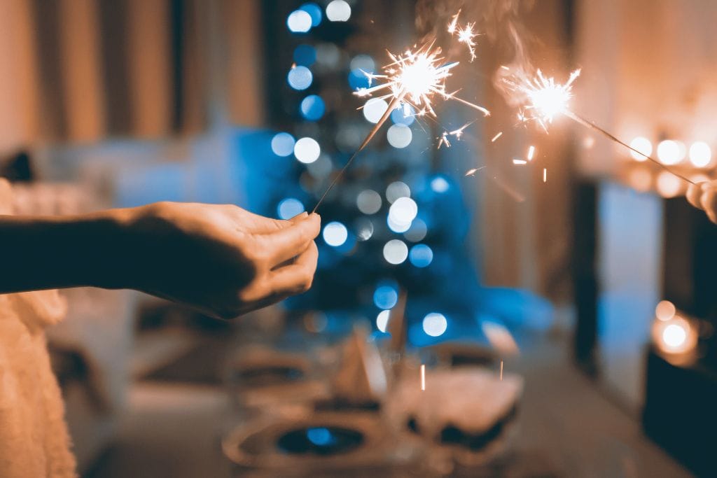 A hand holding sparkler with a Christmas tree in the background. 