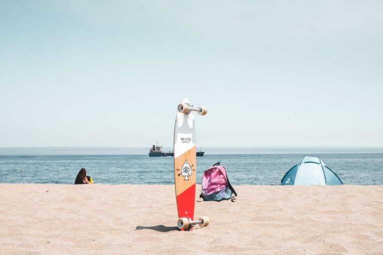 A skateboard dug into the sand upright on the beach.