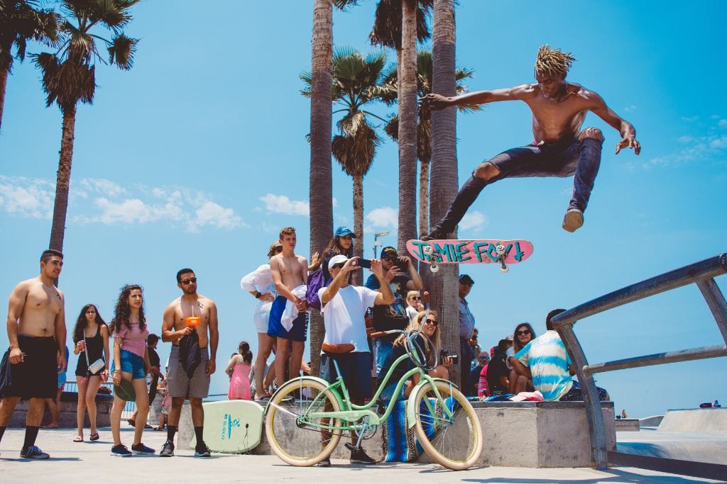 A skateboarder flying through the air while people watch and take photos. Venice, California. 