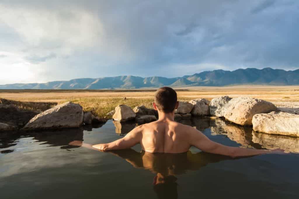A man soaking in a natural hot spring - Wild Willy's Hot Spring - looking at the mountains in the distance.