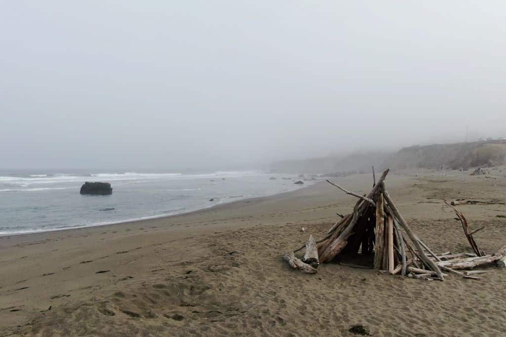 A tent made of sticks on a foggy beach.. 