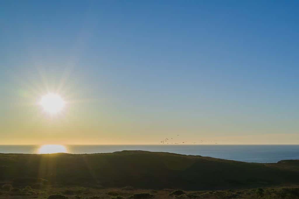 The sun setting over the Pacific Ocean with a cliff in the foreground.