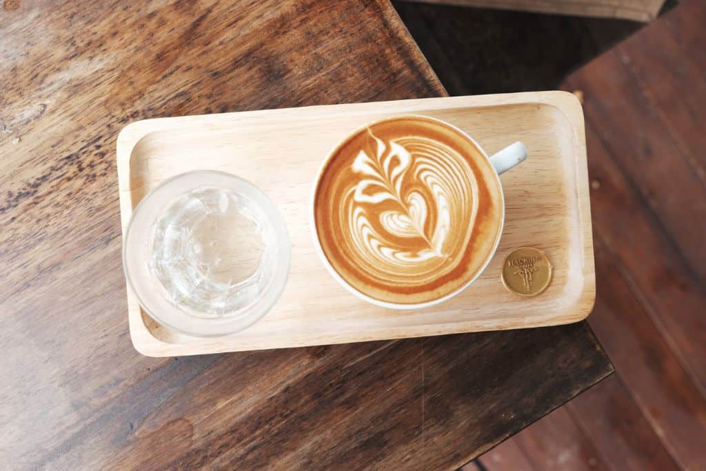 A latte on a wooden dish next to a glass of water.