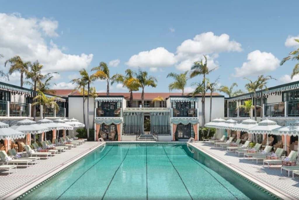 A large swimming pool at a hotel surrounded by palm trees and lounge chairs. 