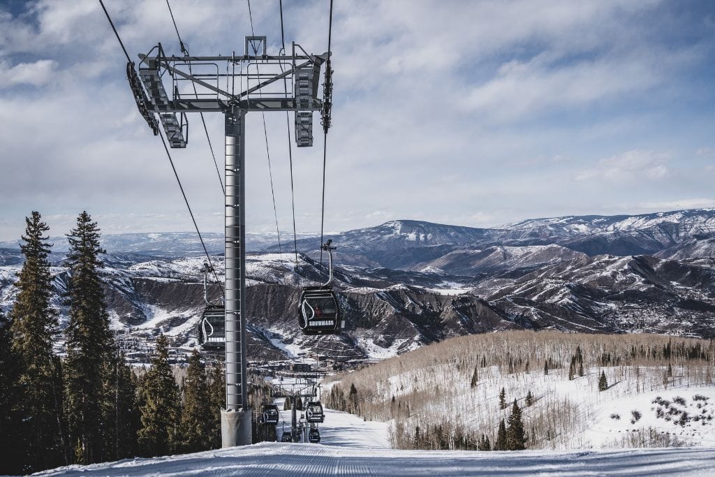 A gondola in mid air with a snowy mountainous background. 