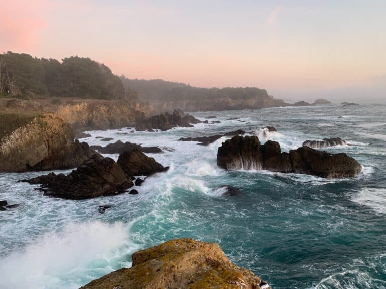 The ocean cashing against rock formations in the sea against a cliff.
