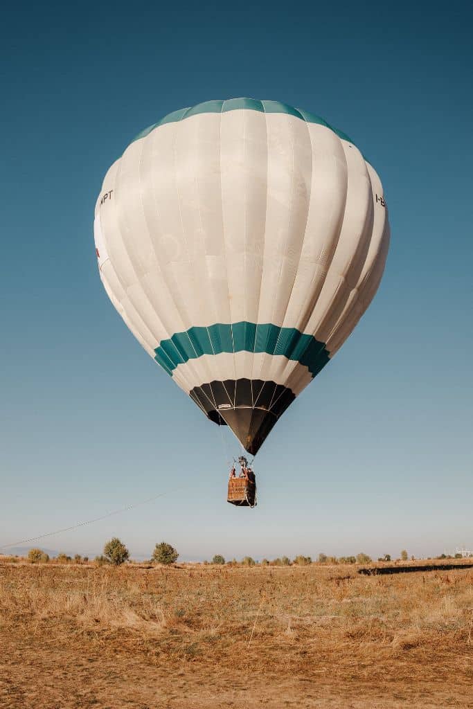 A white hot air balloon with a green stripe ascending to the clouds.