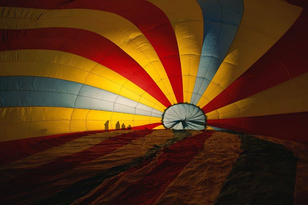 A hot air balloon on its side being blown up with the shadows of four people behind it.