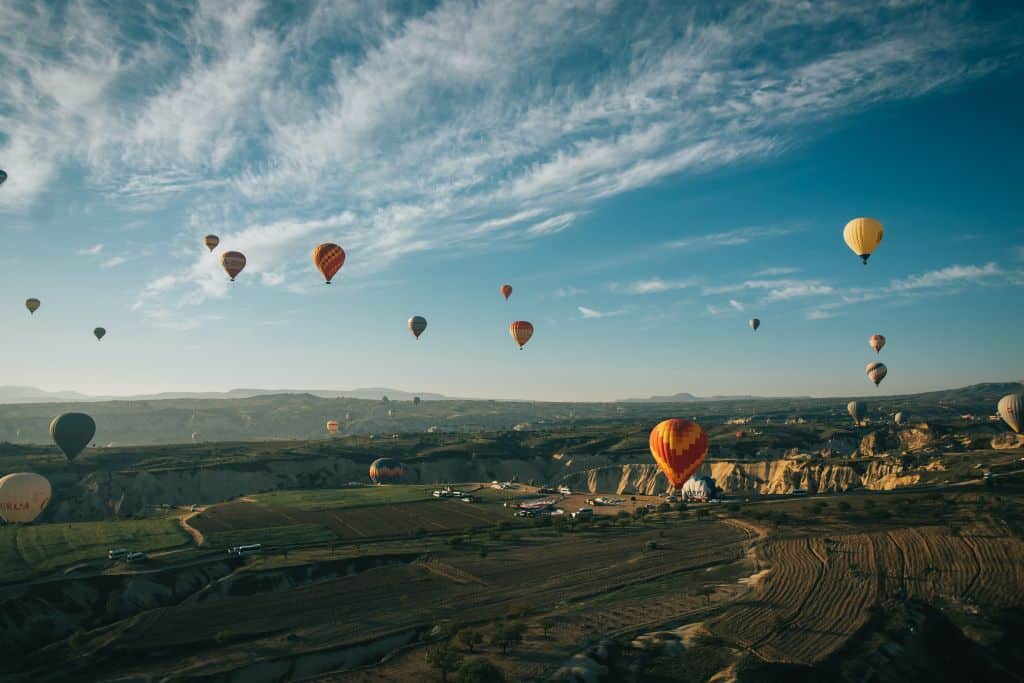 Hot air balloons over fields of trees, mountains, and a body of water in Temecula, California.