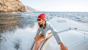 A woman in a red hat smiling while hanging off a speed boat in a lake.