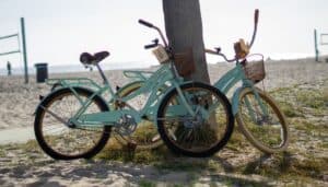 Two turquoise bike leaning against a palm tree at the beach.