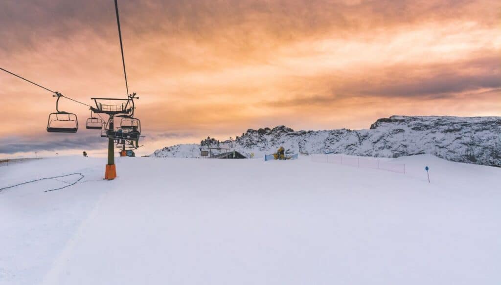 A ski lift at dusk on a snowy mountain.