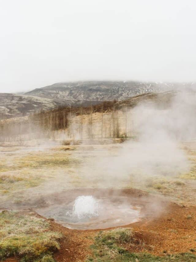 A natural hot springs, a pool of water in a hole in the ground with steam coming out of it.