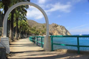A path along water with a torquoise fence and a mountain in the background.