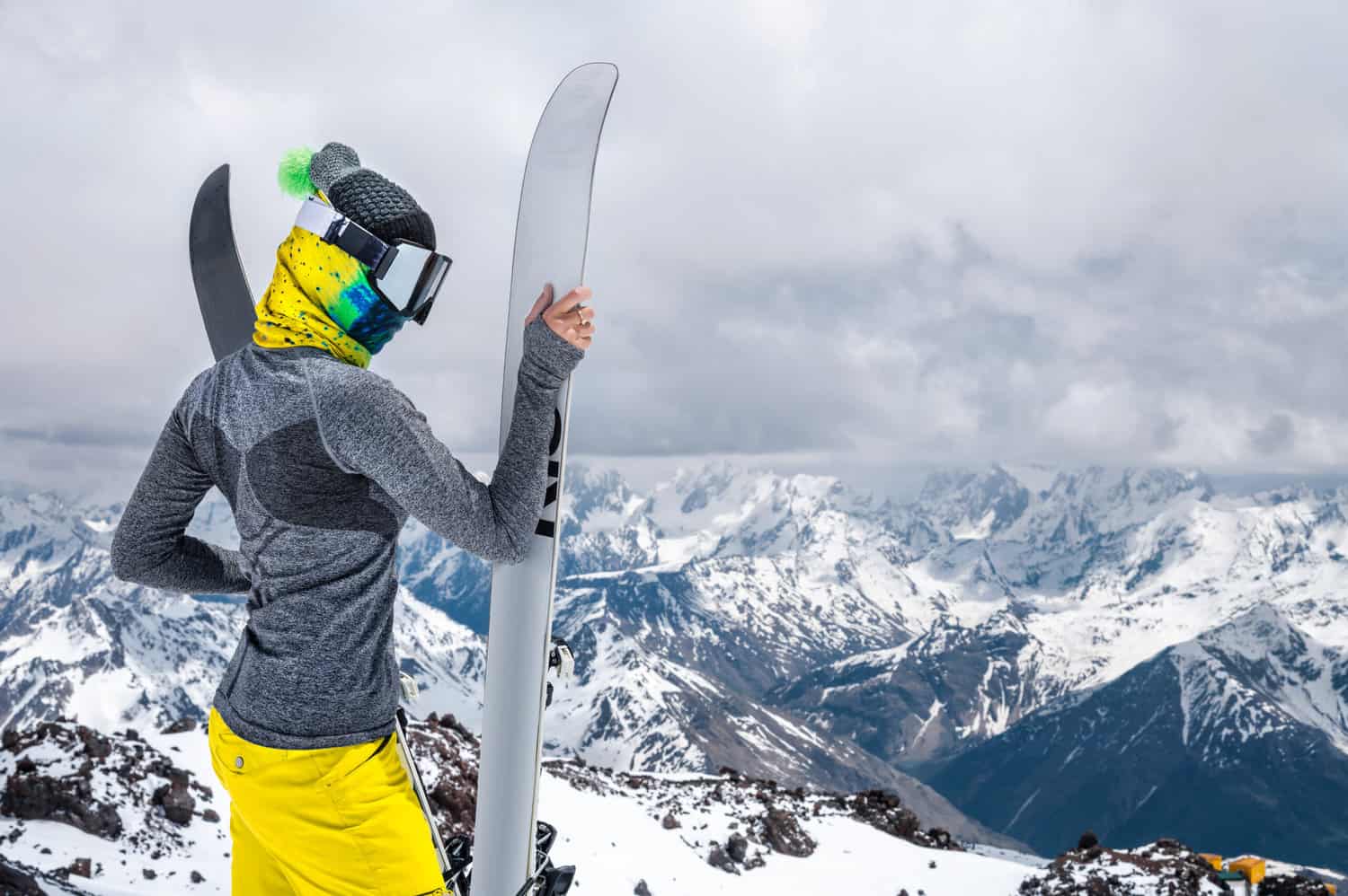 A woman in ski gear holding her skies looks down a steep and snowy mountain. 