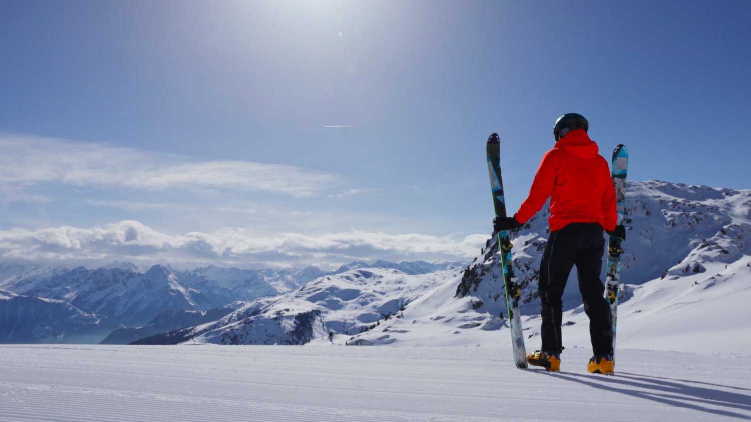 A skier holding his skies looking down a snowy mountain. 