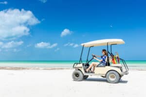 A woman happily driving a golf cart on a beach.