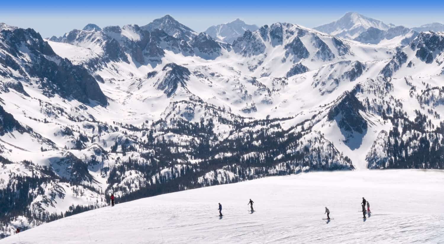 Skiers at the bottom of a large and snow mountain.