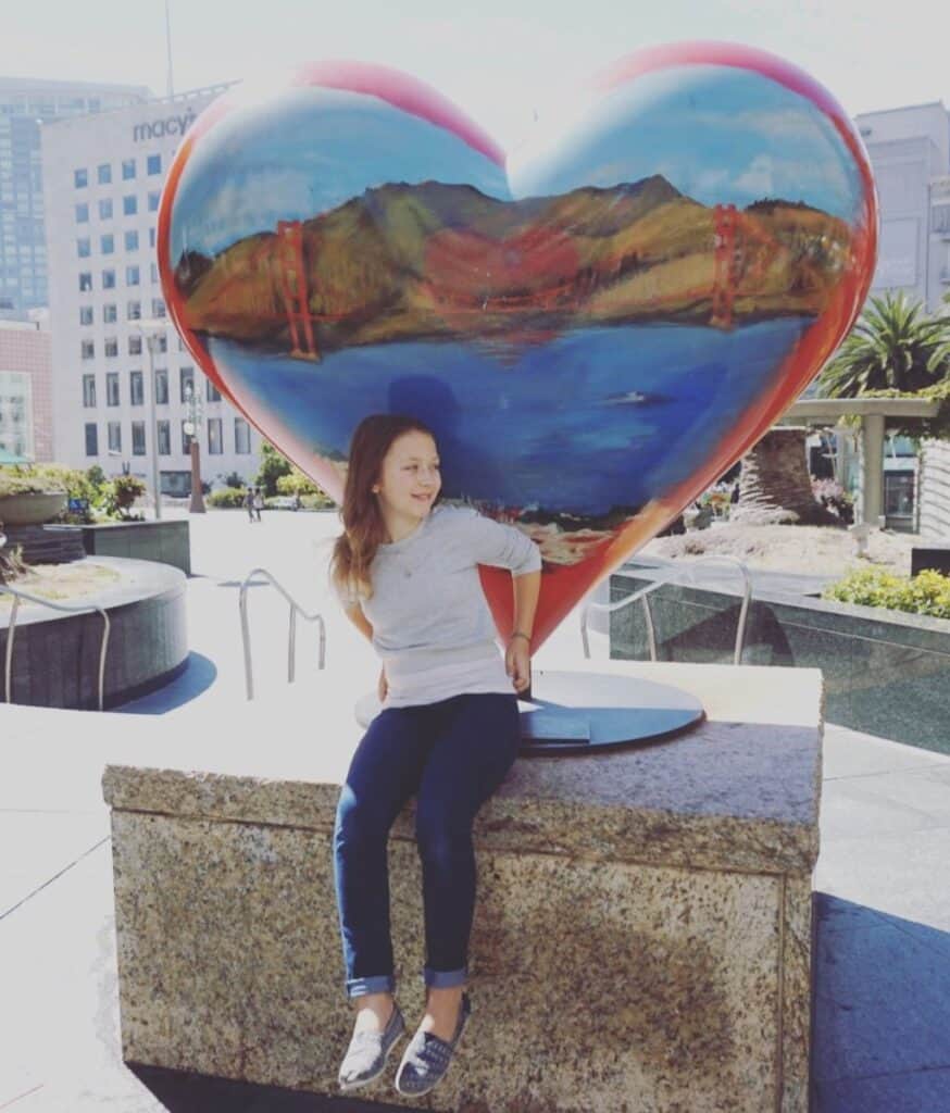 An Adorable little girl sits next to the heart at the heart of Union Square in San Francisco.