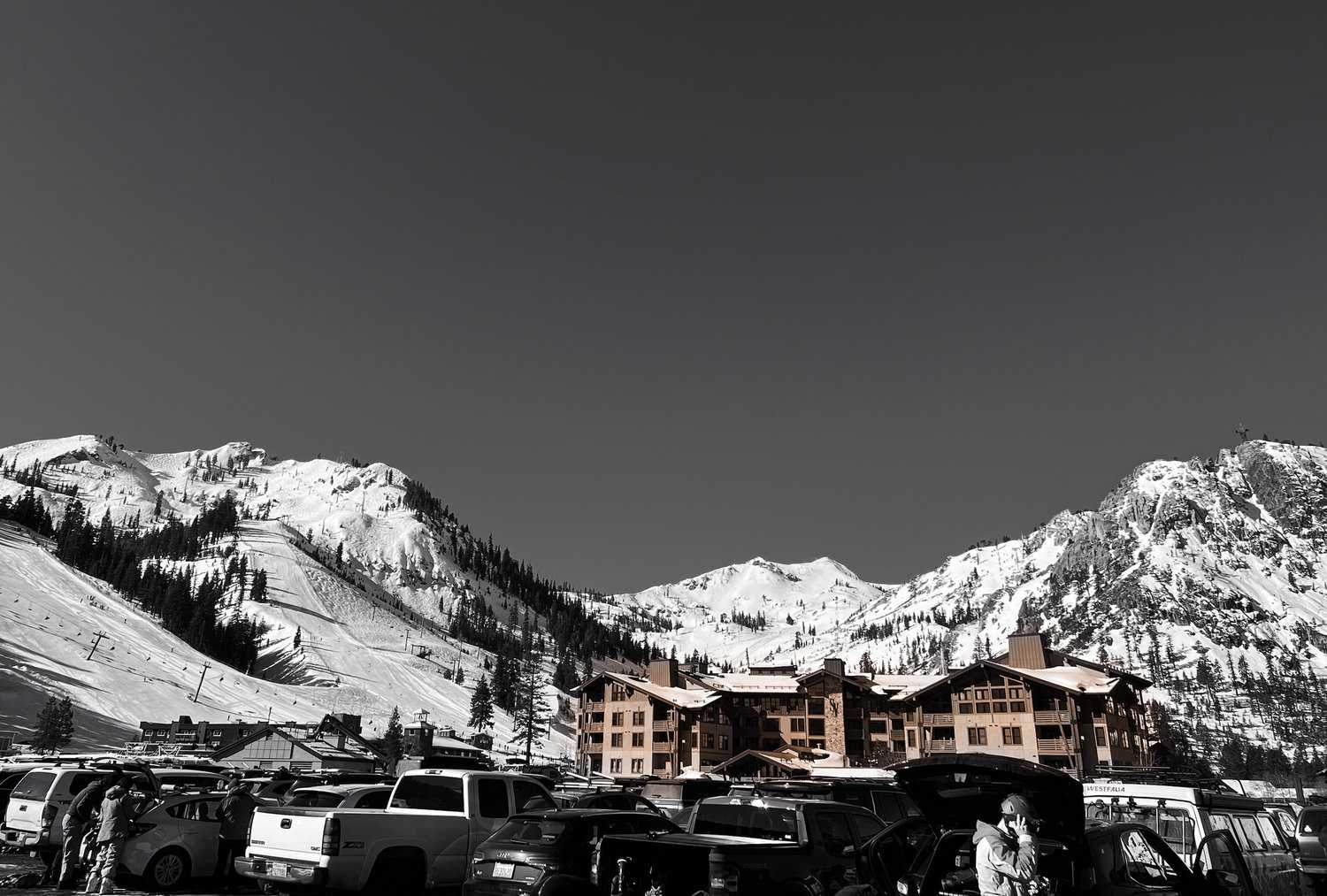 A ski lodge with many cars parked in a front of it and a large, snowy mountain in the background.