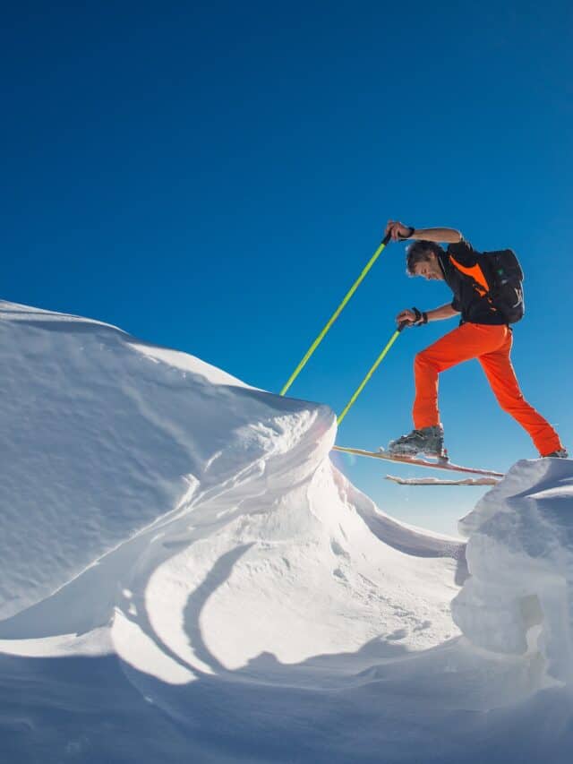 A man with skies on climping from one mountain of snow to another.