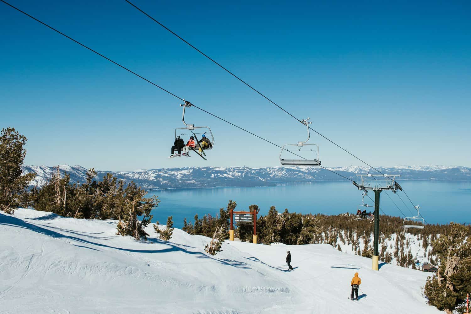 A chair lift at a snowy California ski resort with beautiful Lake Tahoe in the background.