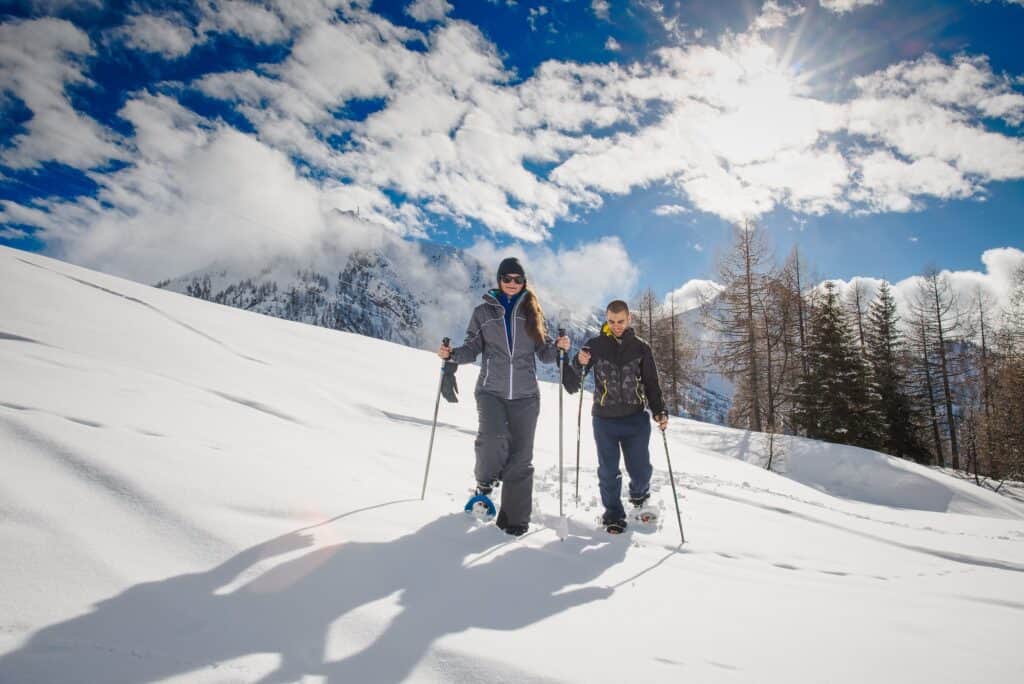 A man and a woman snowshoeing across a mountain of snow.