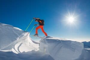 A man with skies on climping from one mountain of snow to another.