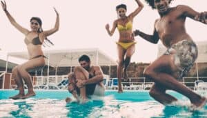 Four people jumping into a pool and having fun.
