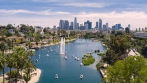 A large large with swan boats in it as well as a fountain with downtown Los Angeles in the background.